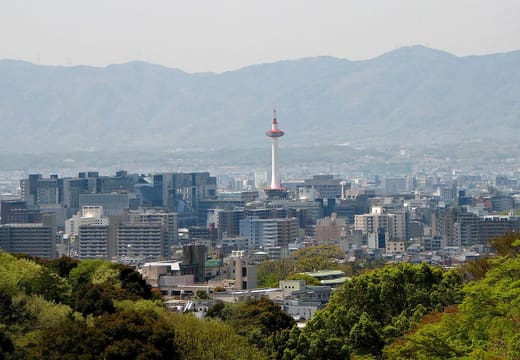 Kyoto Tower rising above the city centre with mountains behind, seen from the east