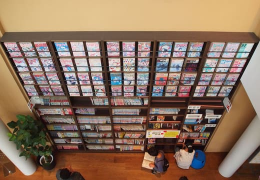 Readers below the tall wall of manga shelves inside the Kyoto International Manga Museum
