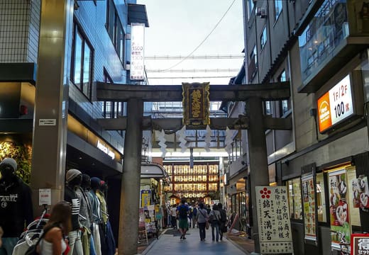The stone torii of Nishiki Tenmangu over the shopping street, with the shrine lanterns beyond, Kyoto