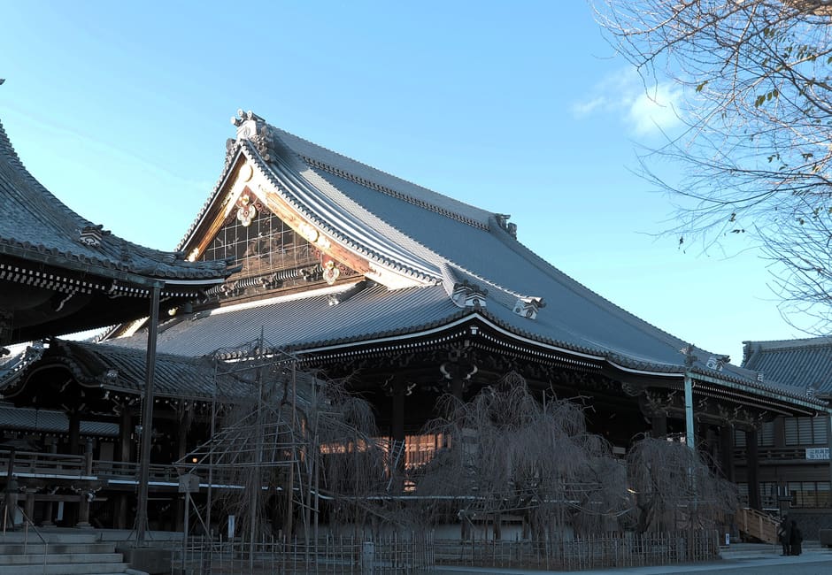 The great tiled roof of the founder's hall at Bukko-ji, with bare weeping cherry trees in front, under a blue sky