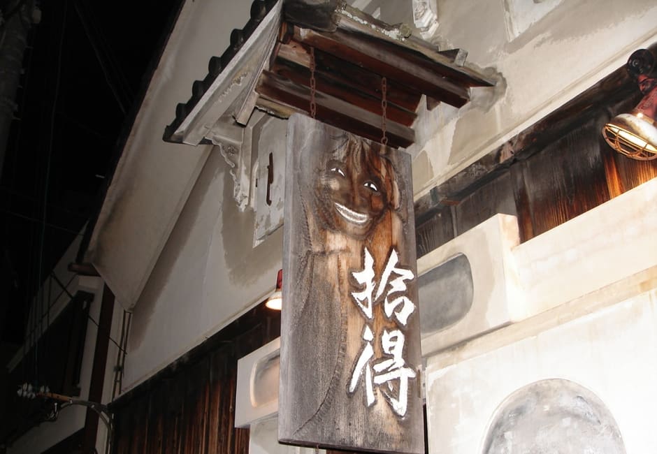 The carved wooden sign of Coffee House Jittoku hanging from the white plaster sake storehouse it occupies on Omiya-dori