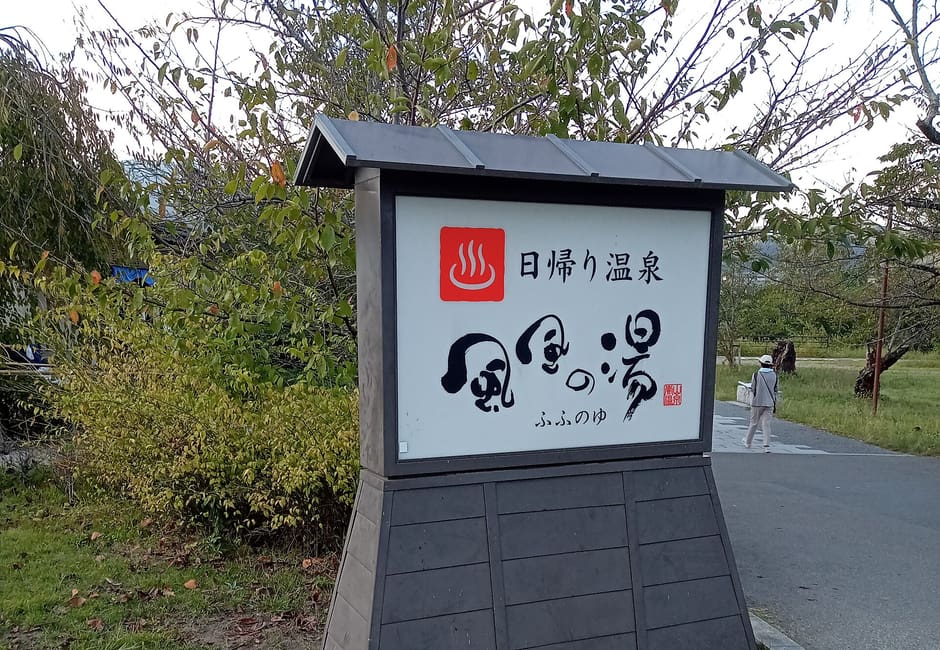 The roadside sign of the Fufu no Yu day spa in Arashiyama, its name brushed beside a hot spring symbol