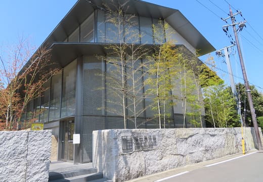 The glass and dark steel front of the Fukuda Art Museum in Arashiyama, with its name plate on the stone wall