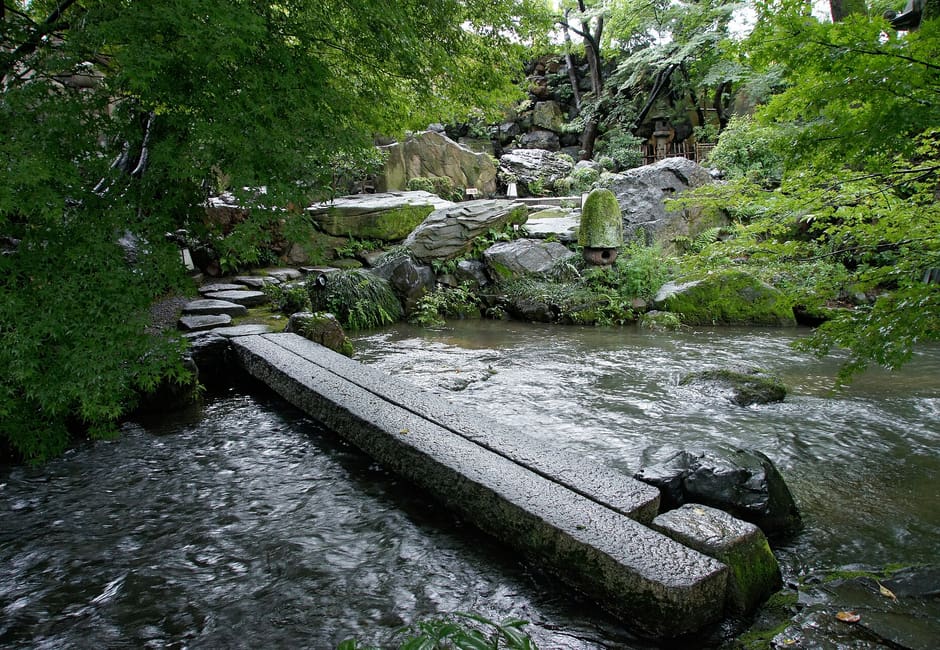 A stone slab bridge over the stream in the green garden of Ganko Takasegawa Nijoen