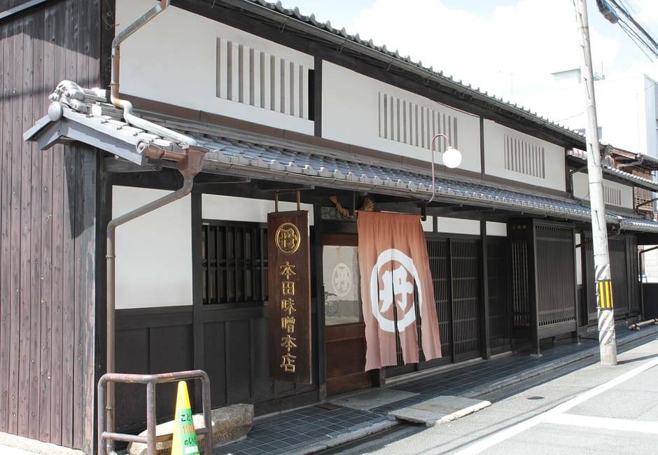 The wooden front of the Honda Miso Honten shop, with its hanging name board and a crested noren over the door