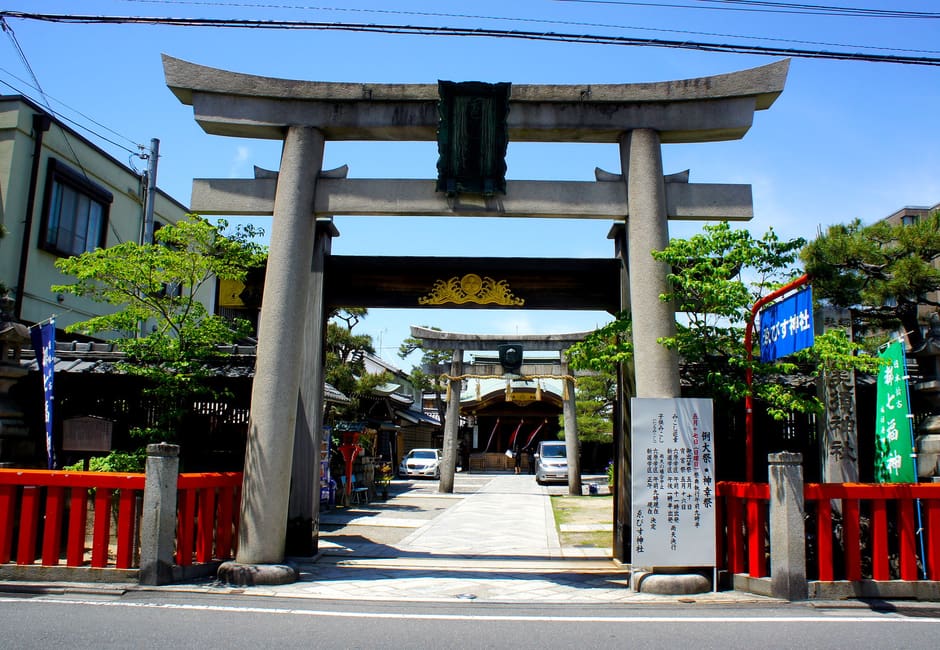 Stone torii of Kyoto Ebisu Shrine on Yamato-oji, with the Ebisu face on the inner gate and the hall beyond