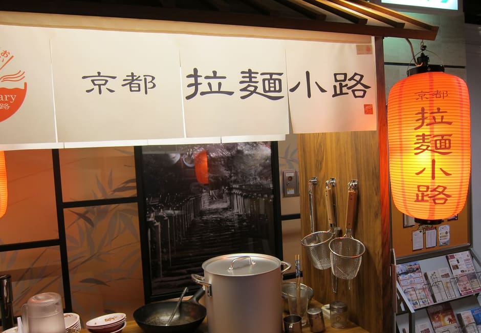 The entrance display of Kyoto Ramen Koji with a noren, a red lantern and a stock pot