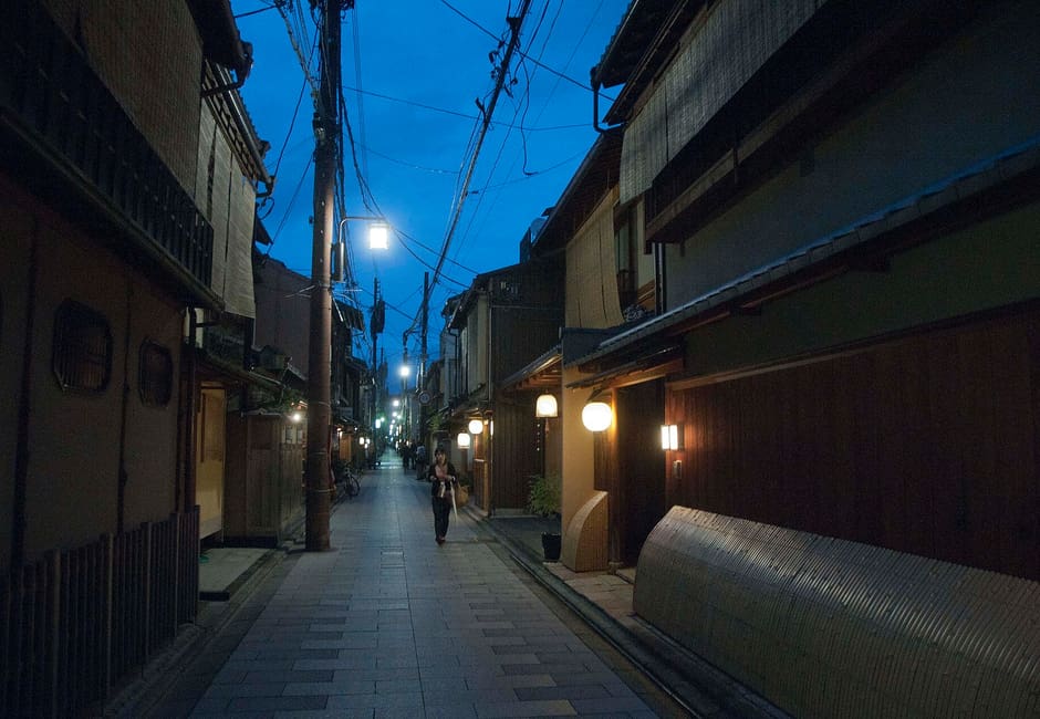 Miyagawacho's stone-paved street at dusk, its teahouse lanterns lit along wooden fronts