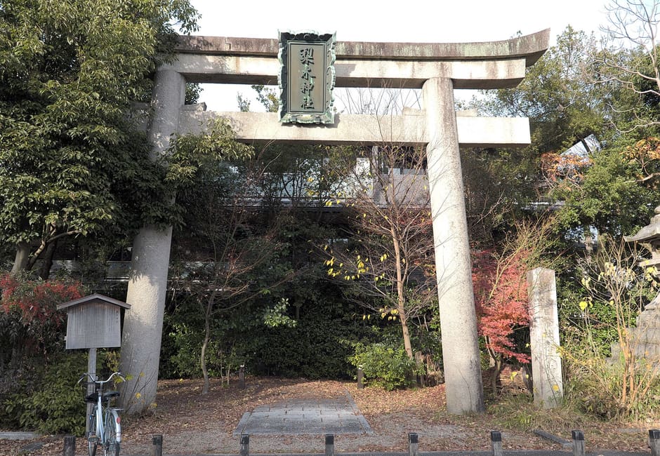The stone torii of Nashinoki Shrine with its name plaque, a wooden notice board and the path into the grounds