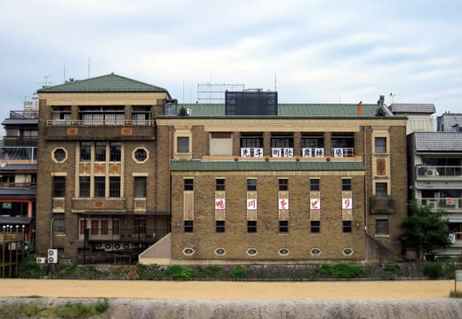 The brick Pontocho Kaburenjo theatre seen from the Kamo River bank, its green tiled roofs above the riverside path